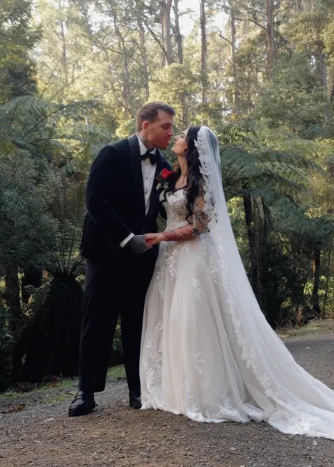 A wedding couple kissing in a sunlit grove